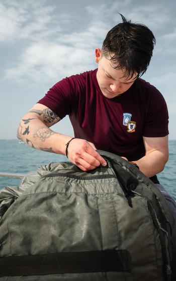 A paratrooper in a red shirt works on his bag.