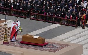 A plain wooden coffin with a cross on it sits on an altar.