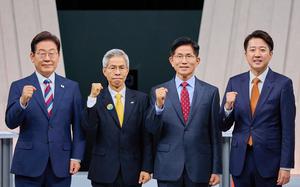 Four men in suits stand side by side on a stage, posing with raised fists. 