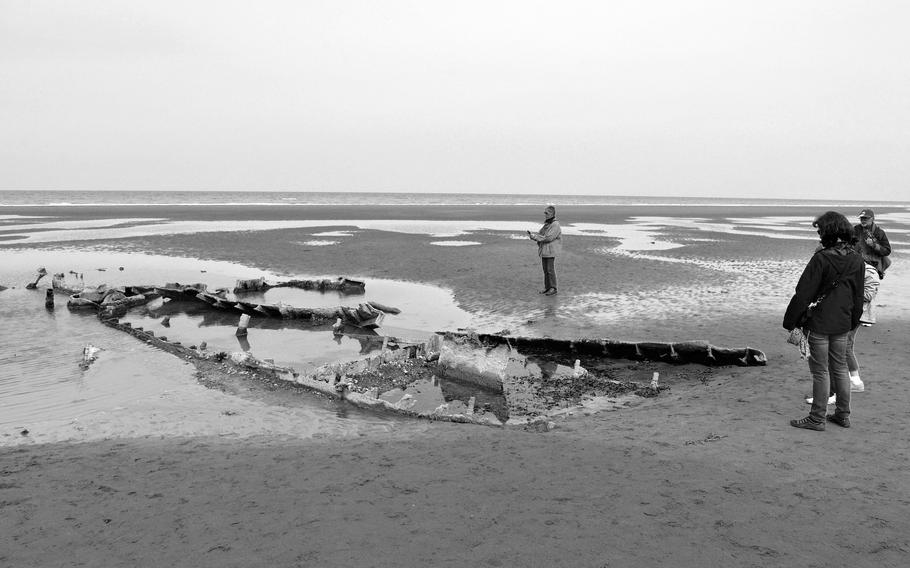 Visitors look at the remains of a world War II landing craft sunk in the sands of Omaha Beach below the Normandy American Cemetery in April 2014.