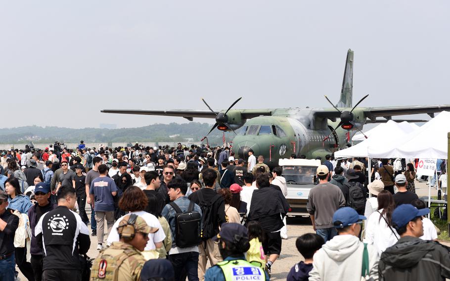 A large transport cargo plane sits on a runway as a crowd of visitors moves around it during an air show.