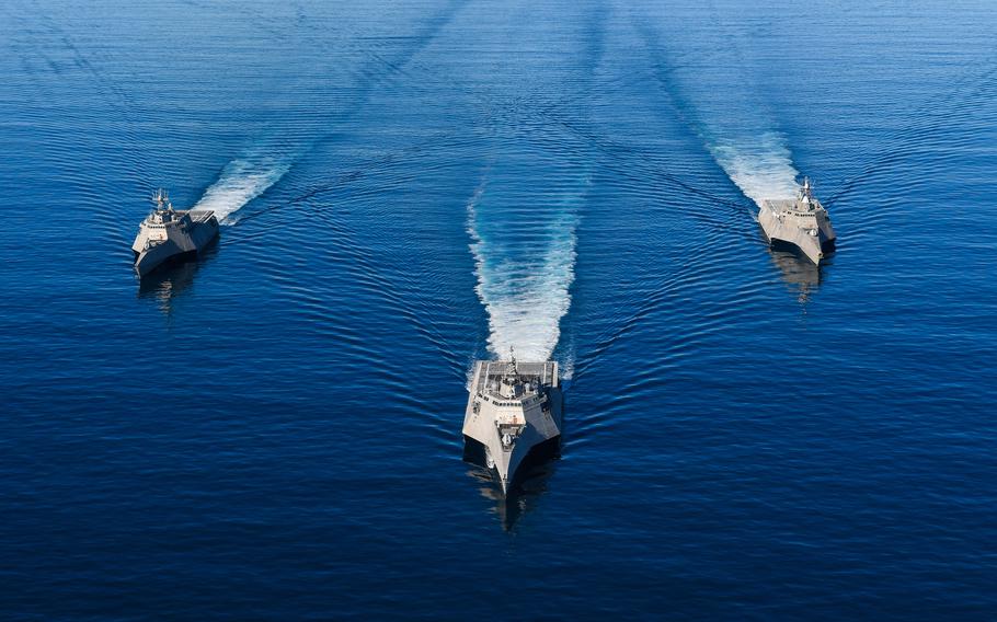 Three ships cruise in the ocean, with their wakes trailing behind.