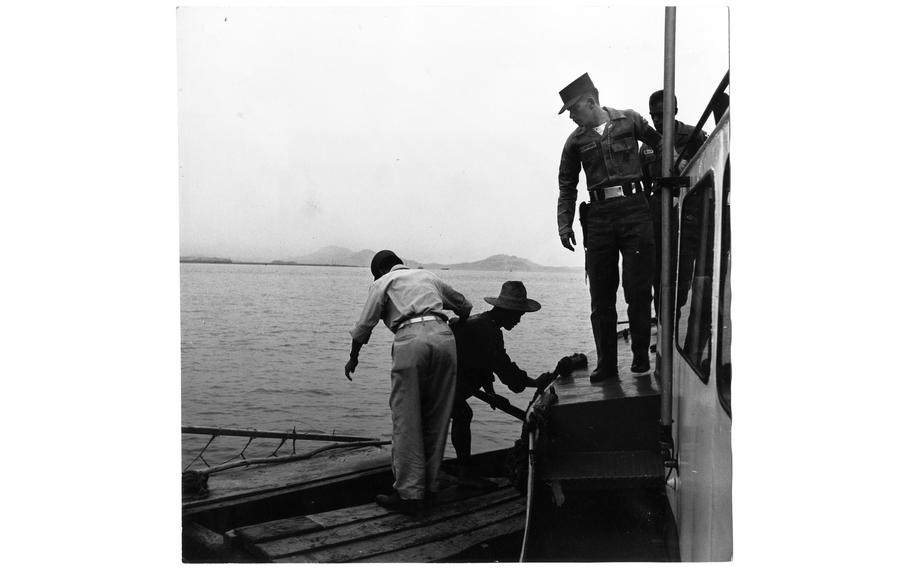 The patrol boat of the 8224th Military Police Detachment stationed in Inchon, South Korea, comes alongside a small Korean boat in Inchon harbor and warns its boatman to move his craft away from the ship unloading area in the harbor. A Korean MP acts as interpreter and boards to check their cargo and harbor pass as PFC Bobby Rutherford looks on.