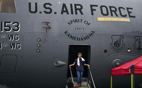 A young man steps out of a C-17 Globemaster II onto stairs. Above the doorway, lettering reads “U.S. Air Force” and “Spirit of Kamehameha.”