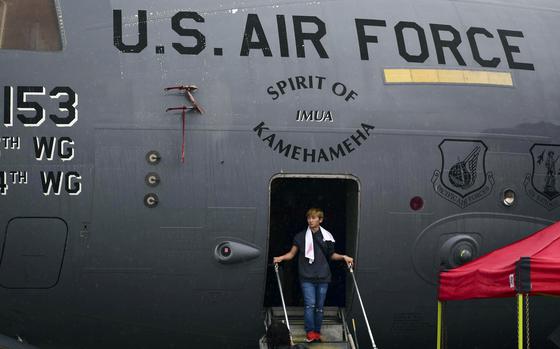 A young man steps out of a C-17 Globemaster II onto stairs. Above the doorway, lettering reads “U.S. Air Force” and “Spirit of Kamehameha.”