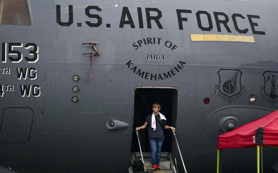 A young man steps out of a C-17 Globemaster II onto stairs. Above the doorway, lettering reads “U.S. Air Force” and “Spirit of Kamehameha.”