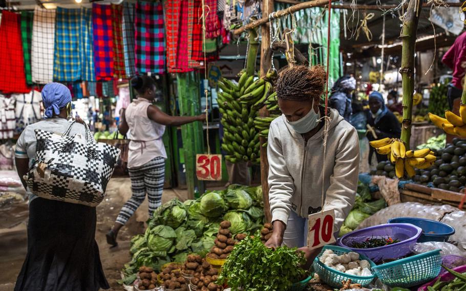 A vendor wearing a protective face mask arranges fresh produce on her vegetable stall at Toi market in Nairobi, Kenya, on May 26, 2020. 