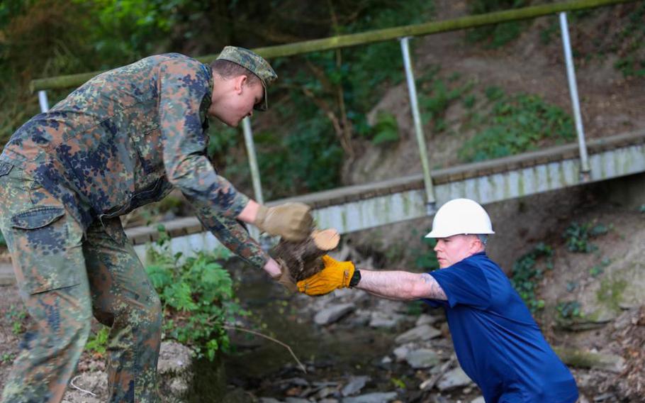 U.S. Army Sgt. Maj. Eric Riding of the 21st Theater Sustainment Command, right, and German Cpl. Andre Beutel lift debris from a stream during a cleanup project in St. Goar, Germany, July 11, 2022. 