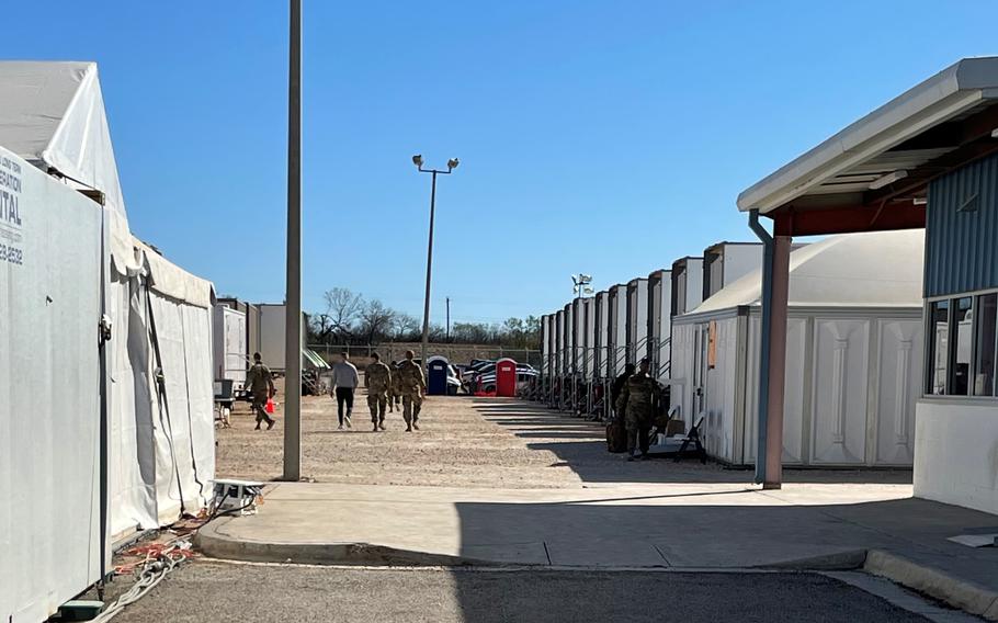 Soldiers walk through a row of bed trailers at Base Camp Walker in Laredo, Texas, on Feb. 13, 2022. Each trailer can house dozens of soldiers in three-tiered bunk beds. 