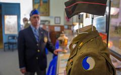 Examining a uniform worn in World War II in 1945 by U.S. Army Cpl. George Eigner, Battery A, 110th Field Artillery (right), is Frank Armiger, national executive director of the 29th Infantry Division Association. His group seeks to preserve the division's yin yang-style patch, now under review by a national commission charged with reviewing names and symbols in the U.S. military.