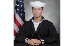 Official Navy photo of Aviation Boatswain’s Mate Jose Antonio Rivera Lynch IV in uniform with an American flag behind his right shoulder.
