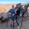 A man and a woman, each wearing hiking gear and holding crutches to support prosthetic legs, pose on a trail in front of a Grand Canyon vista.