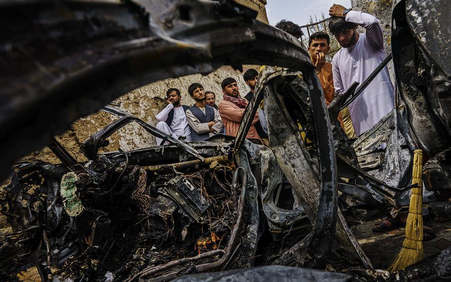 Relatives and neighbors of the Ahmadi family gather Aug. 30, 2021, around the incinerated husk of a vehicle a day after it was hit by a U.S. drone strike in Kabul, Afghanistan. 