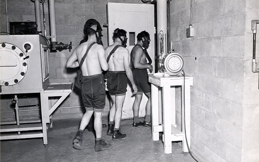 Three men in shorts and no shirts wearing masks enter a chamber.
