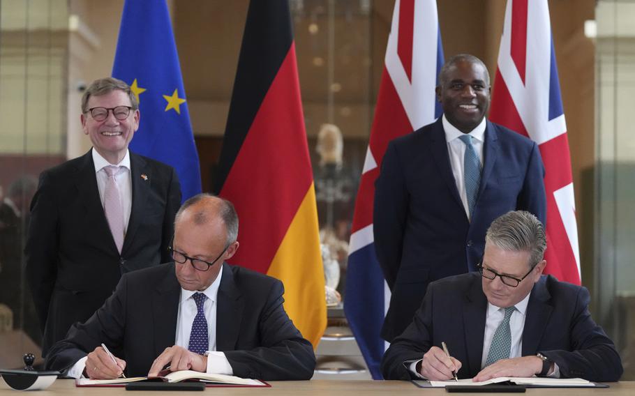 The leaders of Germany and the U.K. in suits, signing papers at a desk.