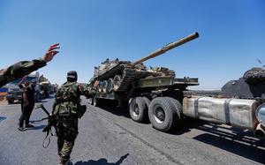 A tank being carried on a truck, with security personnel standing by waving as it goes.