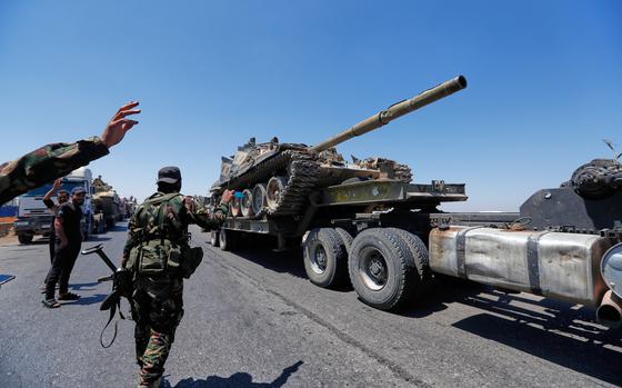 A tank being carried on a truck, with security personnel standing by waving as it goes.