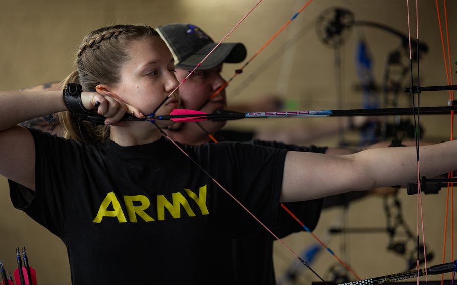 An Army service member drawing her bow to shoot.