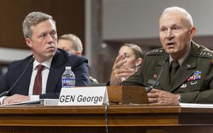 Army Secretary Daniel Driscoll, left, and Gen. Randy George are seated at a table. Driscoll looks at George as the general talks, making a gesture with his right hand.