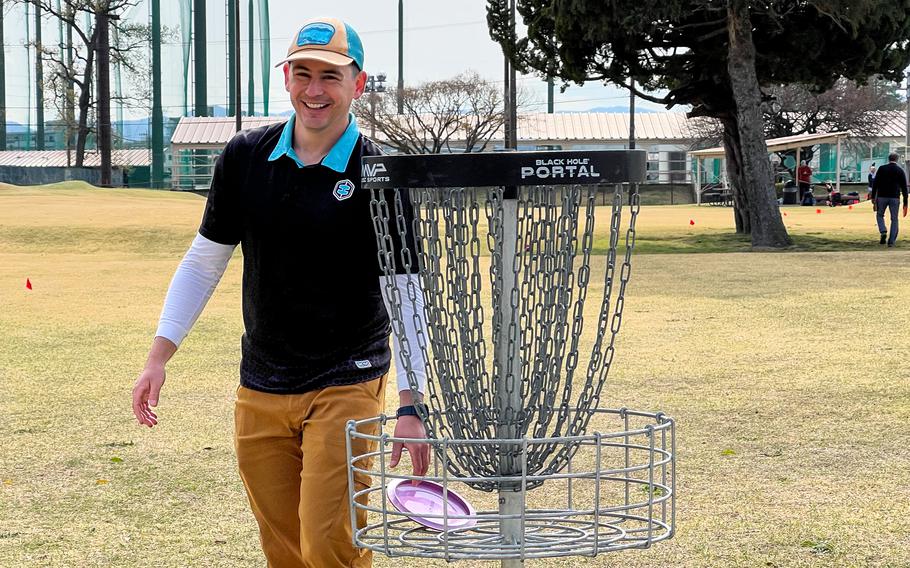 A man collecting a golf disc from a basket.