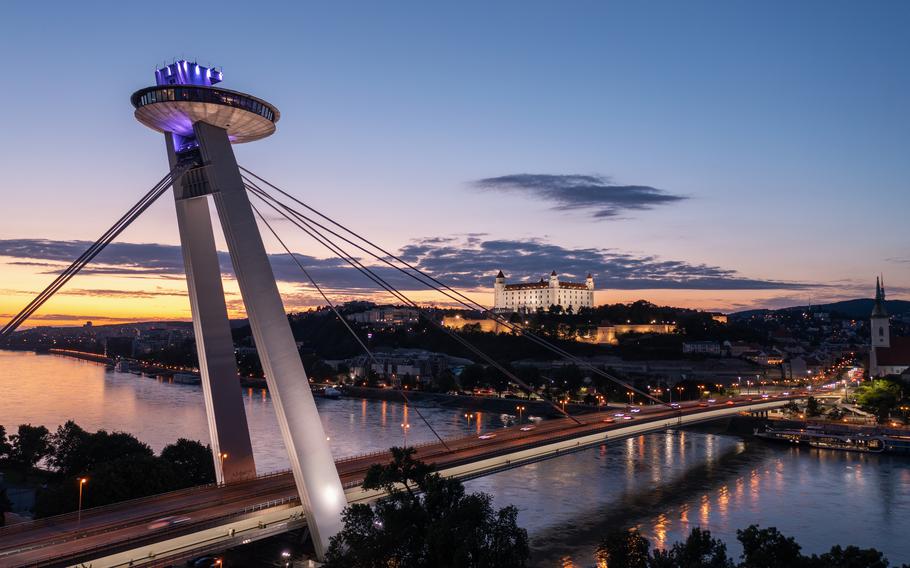 The SNP bridge over the Danube river with night panorama of Bratislava with castle on the hill, Slovakia