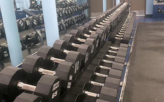 Dumbbells stand ready to use on long racks in a gym.