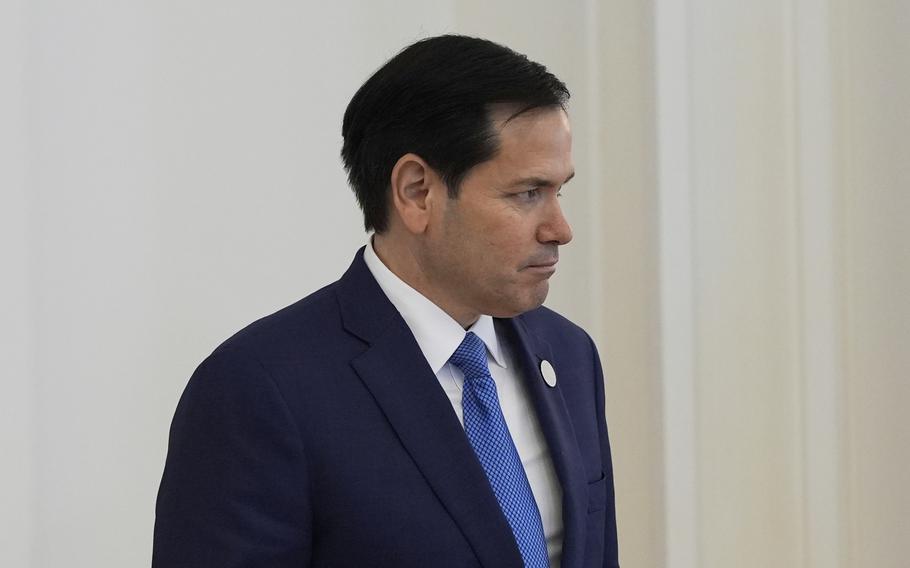 Secretary of State Marco Rubio wearing a suit and blue tie looks off to the side.