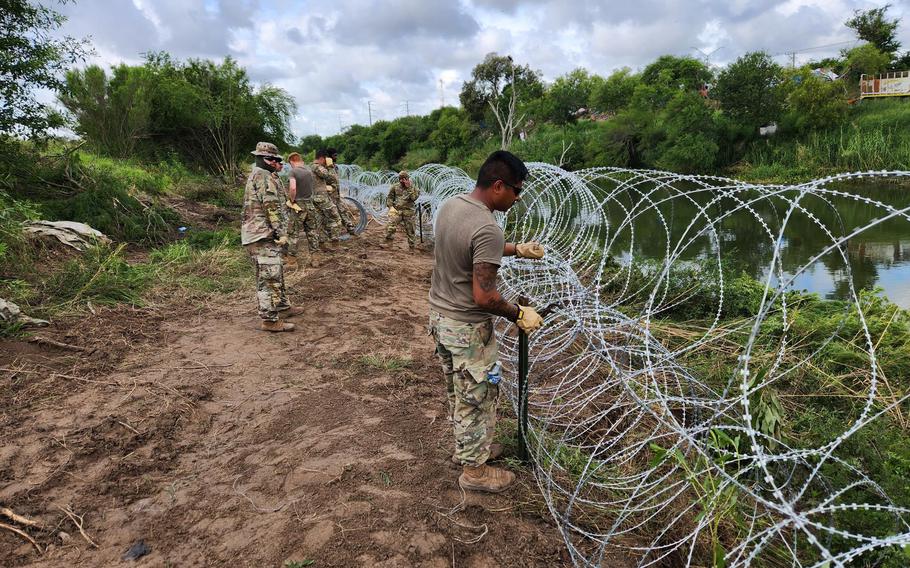 Engineers from the Texas National Guard construct concertina wire barriers on the bank of the Rio Grande in support of Operation Lone Star on May 23, 2023. 