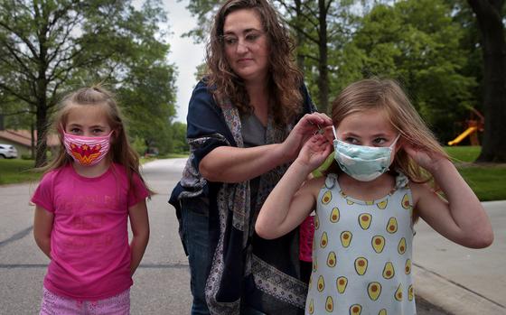 Jenny Berla helps her twins Isla, left, and Elodie with their masks as they approach their sister's school to pick her up after class on Wednesday, May 19, 2021. Berla, who is planning to send the girls to kindergarten this fall, is concerned that dropping mask mandates before young children are eligible for vaccinations leave them open to risk. (Robert Cohen/St. Louis Post-Dispatch/TNS)