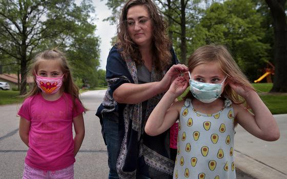 Jenny Berla helps her twins Isla, left, and Elodie with their masks as they approach their sister's school to pick her up after class on Wednesday, May 19, 2021. Berla, who is planning to send the girls to kindergarten this fall, is concerned that dropping mask mandates before young children are eligible for vaccinations leave them open to risk. (Robert Cohen/St. Louis Post-Dispatch/TNS)