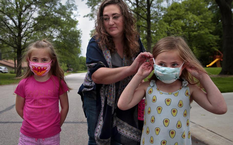 Jenny Berla helps her twins Isla, left, and Elodie with their masks as they approach their sister's school to pick her up after class on Wednesday, May 19, 2021. Berla, who is planning to send the girls to kindergarten this fall, is concerned that dropping mask mandates before young children are eligible for vaccinations leave them open to risk.