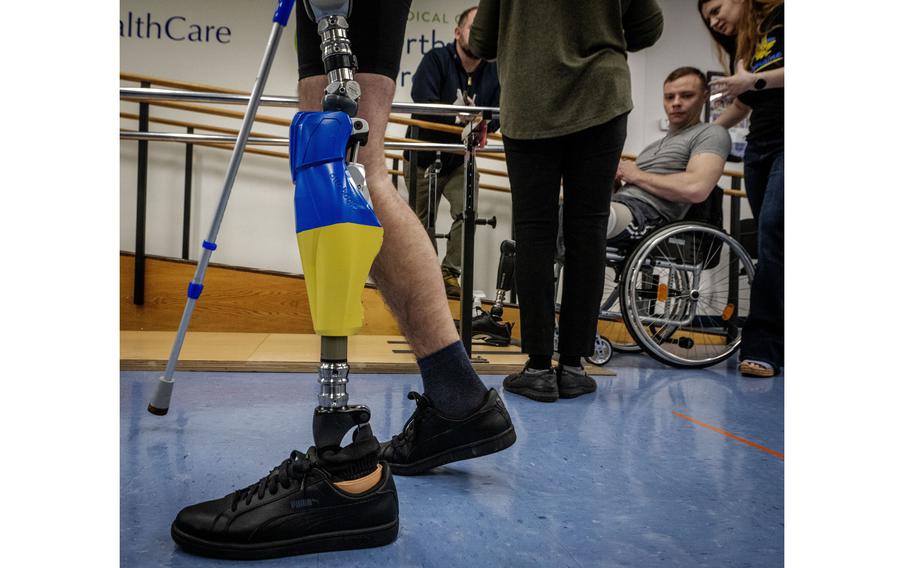 Aleksander Fedun, one of the Ukrainian soldiers getting replacement limbs at Medical Center Orthotics and Prosthetics in Silver Spring, Md., watches his colleague Ruslan Tyshchenko practice walking on his new prosthetic, customized with Ukrainian flag colors.