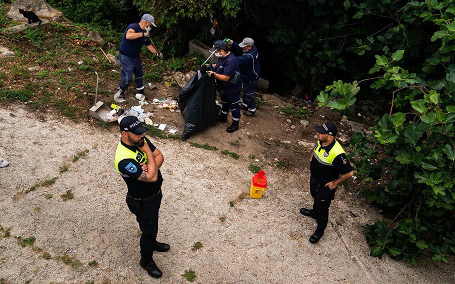 Police escort municipal workers as they remove trash and used syringes in Porto.