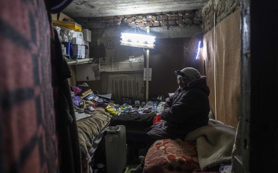 Lubov Gazhla, 62, wears a headlamp as she sits on the bed in the tiny room she is living in underground in the basement of her apartment building in Lyman.