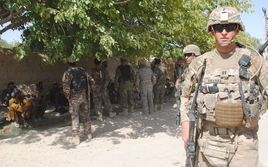 A soldier in the foreground with other troops in the background along a wall.