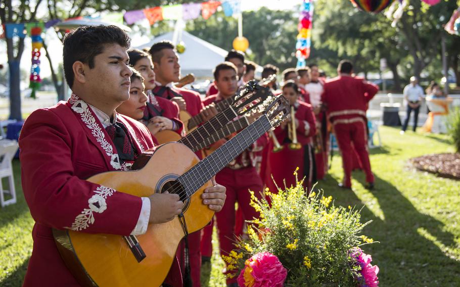 Members of a mariachi band in bright red outfits line up outside on a sunny day.