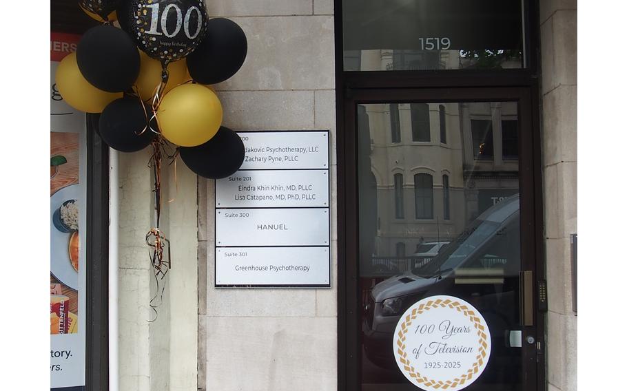 A door adorned by a circular sign reading “100 Years of Television” and balloons.