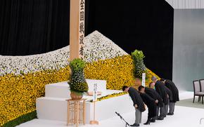 Several men in formal attire bow before a shrine.
