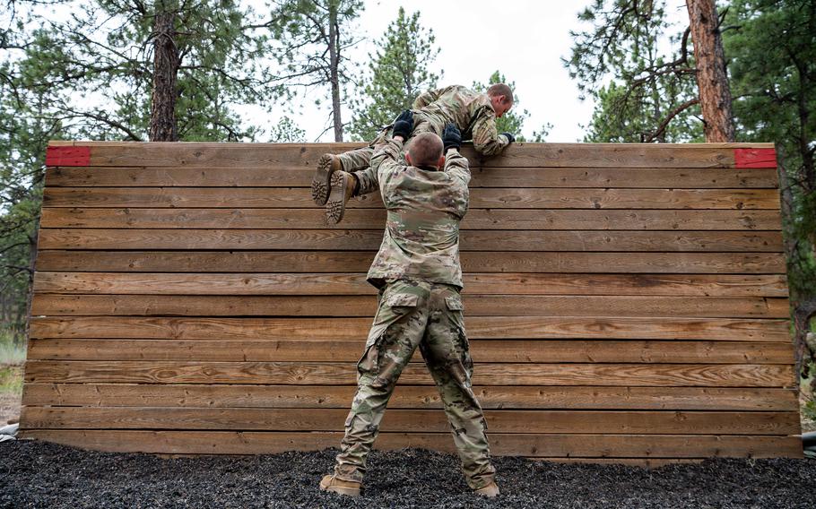 An instructor helps a cadet climb over a wall