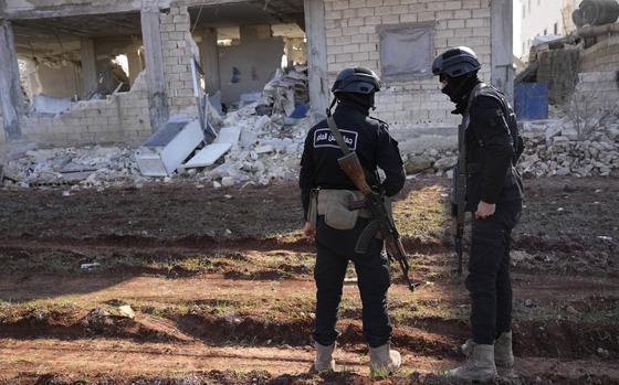 Militants of the al-Qaida-linked Hayat Tahrir al-Sham organization stand in front of a destroyed house in Atareb, Syria, Sunday, Feb. 12, 2023. The man known as Abu Mohammed al-Golani, the leader of Hayat Tahrir al Sham, is trying hard to distance his group from its al-Qaida origins, spreading a message of pluralism and religious tolerance.