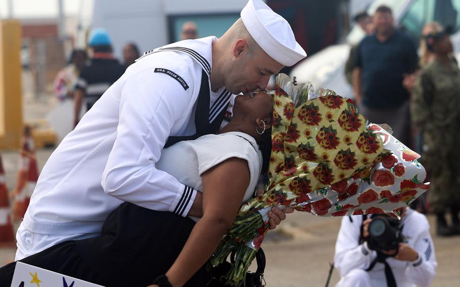 A sailor in uniform embraces and smooches a woman.