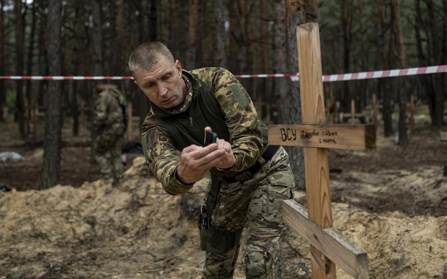 Oleg Kotenko, the Commissioner for Issues of Missing Persons under Special Circumstances, uses his phone to film the grave a Ukrainian soldier in the recently retaken area of Izium, Ukraine, Thursday, Sept. 15, 2022. A mass grave of Ukrainian soldiers and unknown buried civilians was found in the forest of recently recaptured city of Izium. 