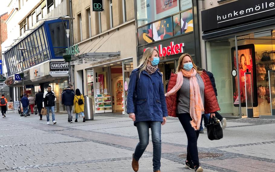 People wearing masks walk past shops in the pedestrian zone of Kaiserslautern, Germany, on March 23, 2021. 