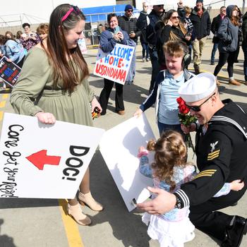 A sailor kneels to talk to his young daughter, with his wife and son standing alongside. 