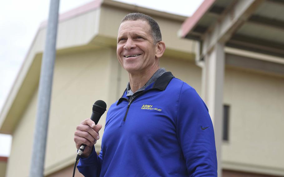 Michael Grinston smiles and holds a microphone as he speaks to U.S. soldiers at a military base.