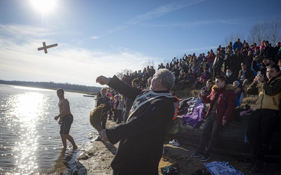 A priest throws a wooden cross in the Danube river during Epiphany celebrations in Facaieni, eastern Romania, Thursday, Jan. 6, 2022. Villagers gather to be blessed with holy water then watch youngsters compete to retrieve the cross from the river. 
