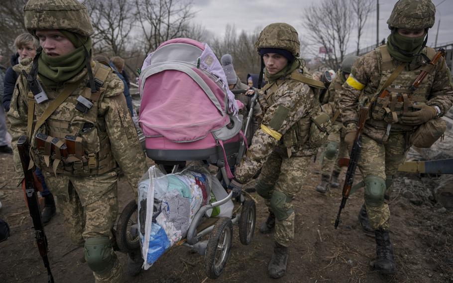 Ukrainian service members carry a baby stroller after crossing the Irpin river on an improvised path under a bridge that was destroyed by a Russian airstrike, while assisting people fleeing the town of Irpin, Ukraine, Saturday, March 5, 2022. 