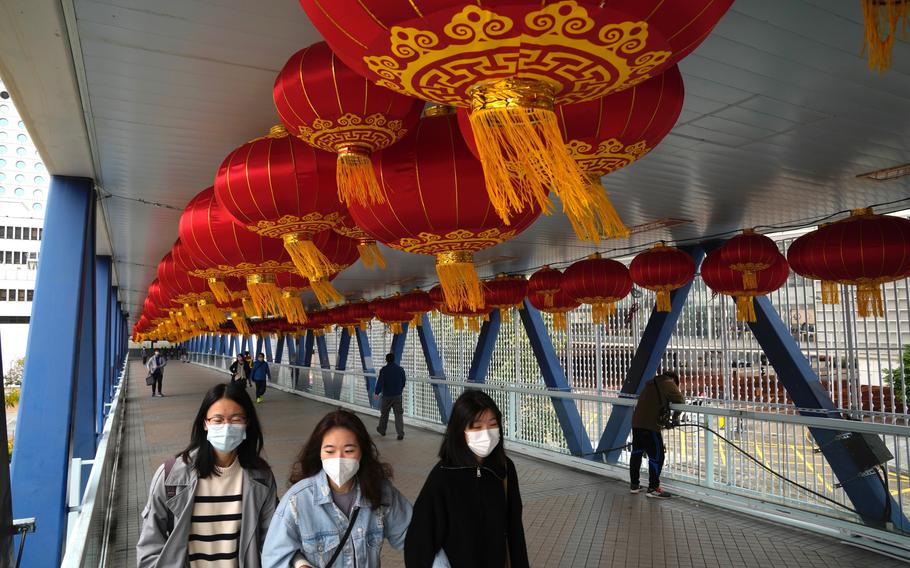 People wearing face masks, walk past decorations on a bridge to celebrate the Lunar New Year in Hong Kong, Tuesday, Jan. 18, 2022. Hong Kong police arrested two former flight attendants for allegedly leaving their homes when they should have been in isolation for possible coronavirus infections, which were later confirmed. 