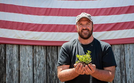 A man standing in front of an American flag holds an oregano seedling in his hands.