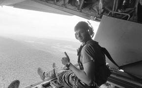 A man gestures while sitting near an opening of an aircraft in the air.